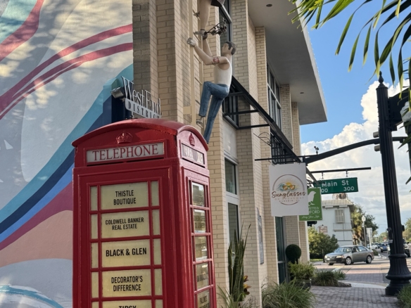 Red telephone booth beside a colorful mural, shops, and palm trees near Main Street in downtown Dunedin, Florida.