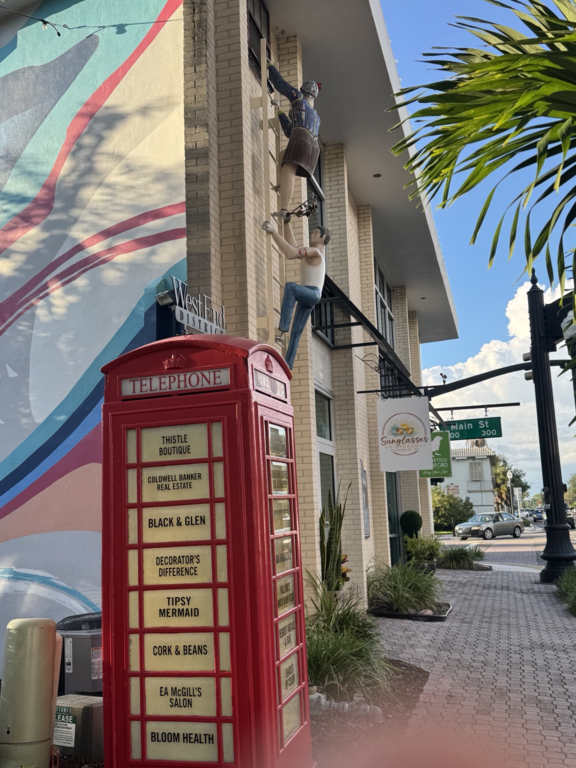 Red telephone booth beside a colorful mural, shops, and palm trees near Main Street in downtown Dunedin, Florida.